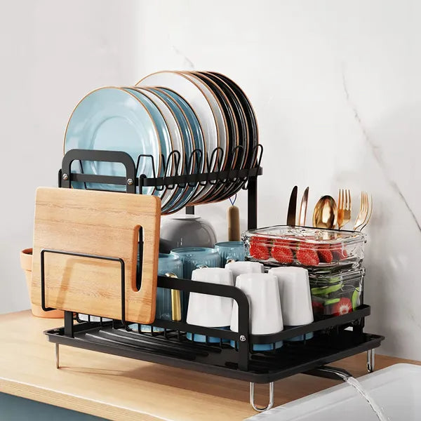 Black 2-tier dish drying rack with drainboard, holding plates, cups, utensils, and a cutting board.