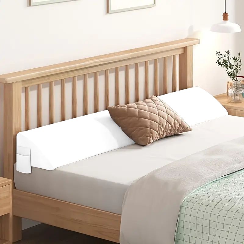 White ergonomic bed gap pillow with side pocket, bridging mattress and wooden headboard.