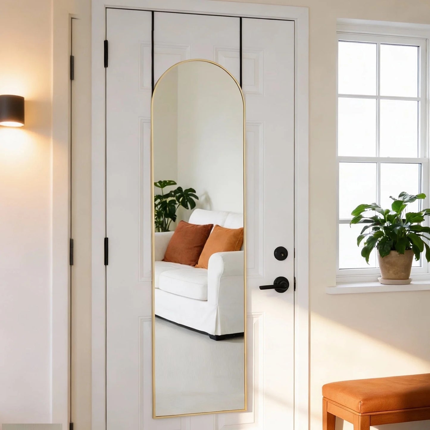 Gold arched full-length mirror hanging over a white door, reflecting a living room.