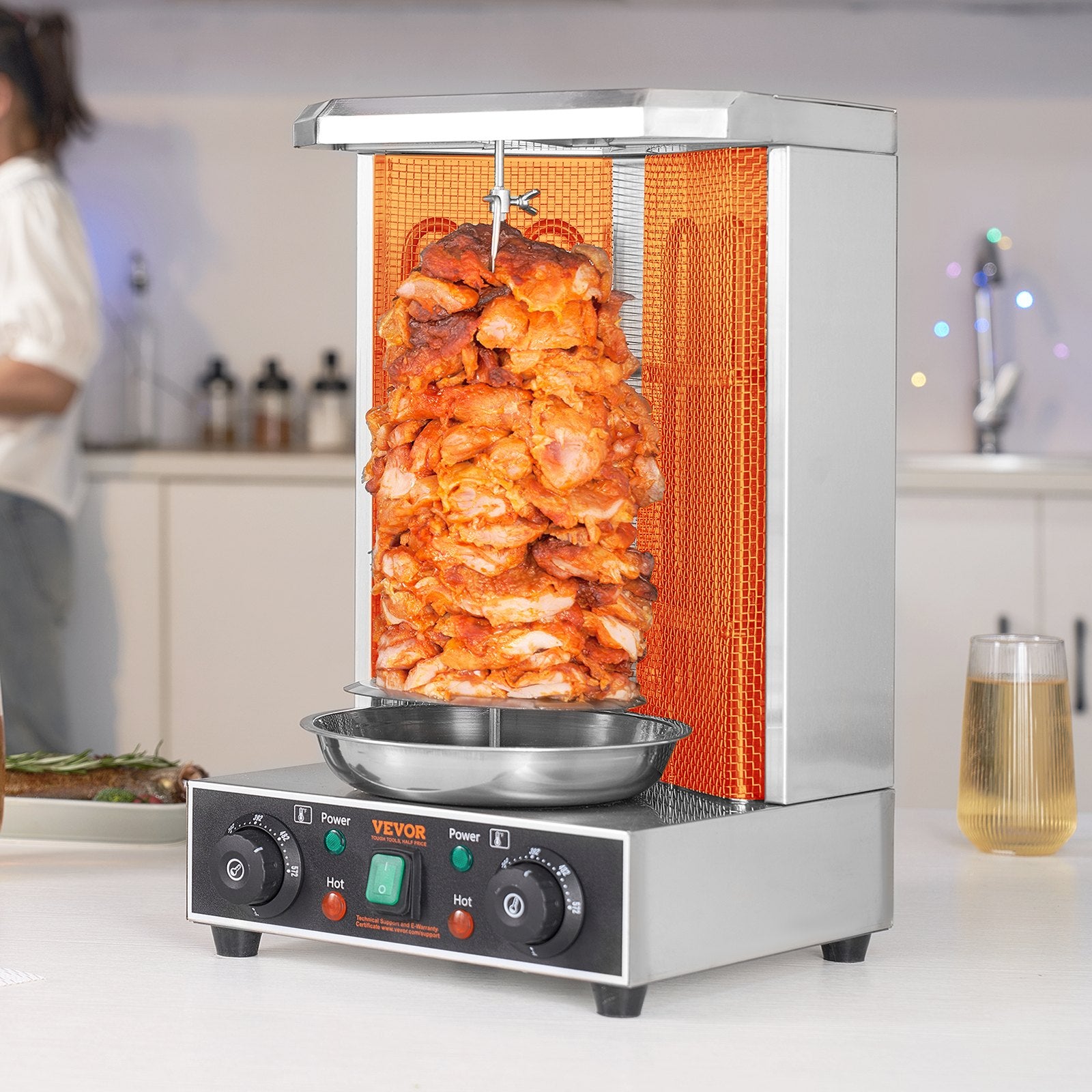 Silver stainless steel vertical broiler with a large rotating skewer of cooking chicken shawarma.