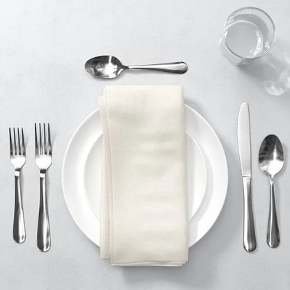 Modern 20-piece mirror-polished stainless steel silverware set with white plate, napkin, and glass.