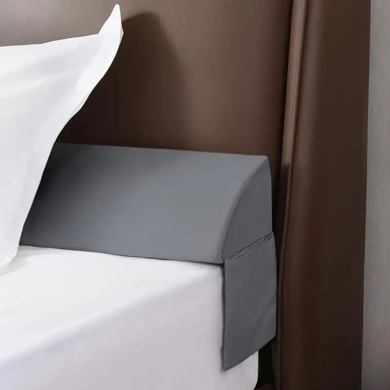 Gray ergonomic mattress gap filler wedge between white sheets and brown headboard.