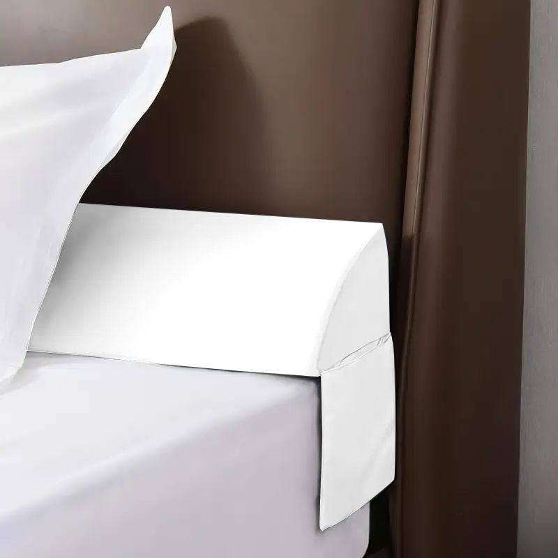 White ergonomic mattress gap pillow bridging a bed and brown headboard, with a white pillow.