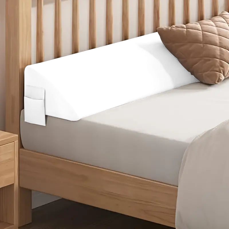 White ergonomic bed gap pillow with side pocket, bridging mattress and wooden headboard.
