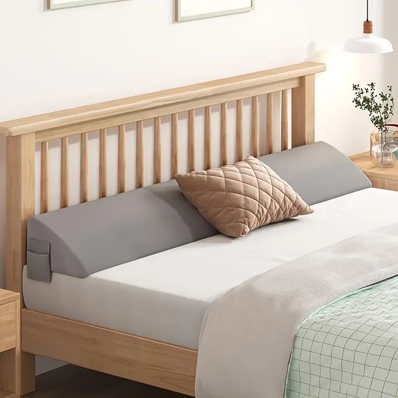 Gray ergonomic mattress gap filler with side pocket on a wooden bed, preventing items from falling.