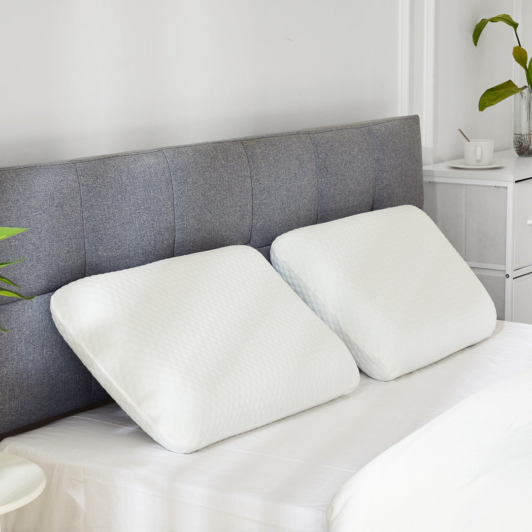 Two white orthopedic memory foam pillows with textured covers on a bed with a gray headboard.