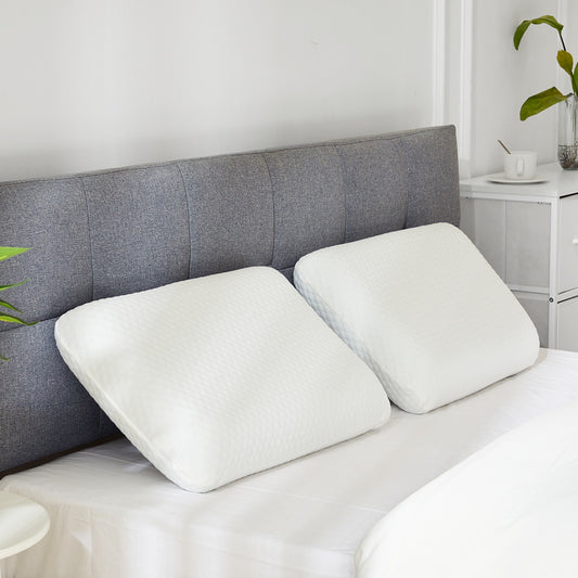 Two white orthopedic memory foam pillows with textured covers on a bed with a gray headboard.