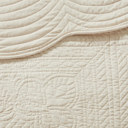 Close-up of a cream reversible scalloped edge quilt with intricate quilted patterns and textures.
