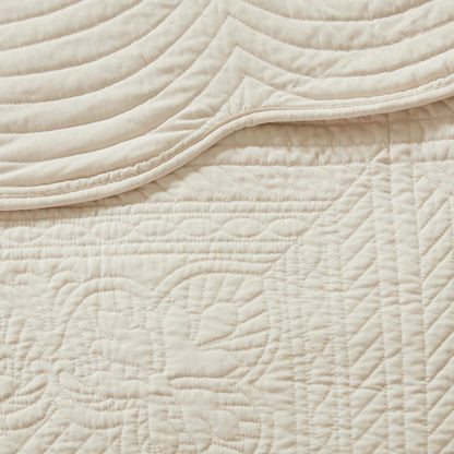 Close-up of a cream reversible scalloped edge quilt with intricate quilted patterns and textures.
