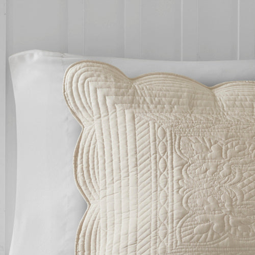 Close-up of a cream scalloped edge quilted pillow sham with intricate stitching on a white pillow.