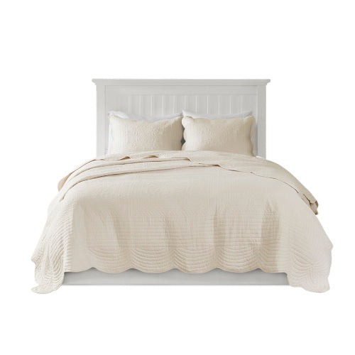 Elegant cream reversible quilt set with scalloped edges and two matching pillow shams on a white bed.
