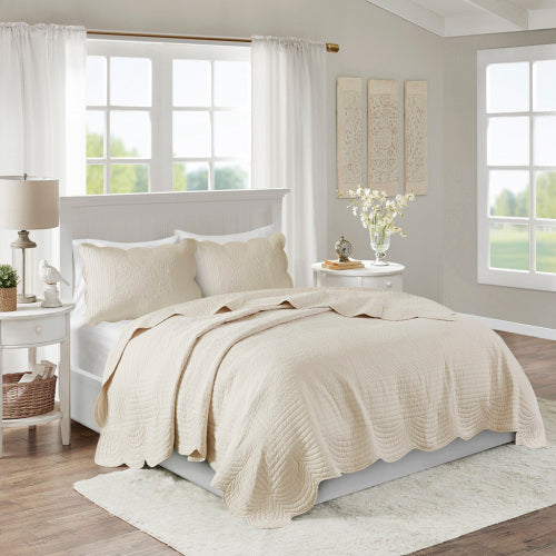 Cream reversible scalloped edge quilt set on a bed with two matching pillow shams.
