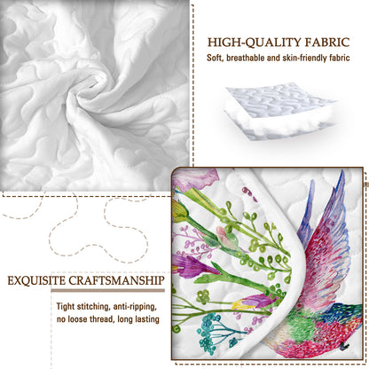 Close-up of a white quilted fabric with a watercolor hummingbird and floral pattern, highlighting soft texture and stitching.