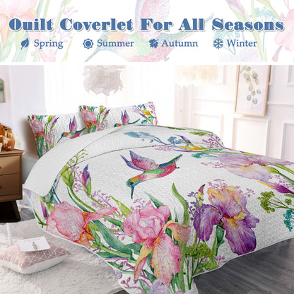 White watercolor hummingbird and floral quilt set with two matching shams on a bed.