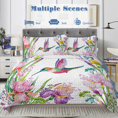 White watercolor hummingbird and floral quilt set with two matching shams on a bed.