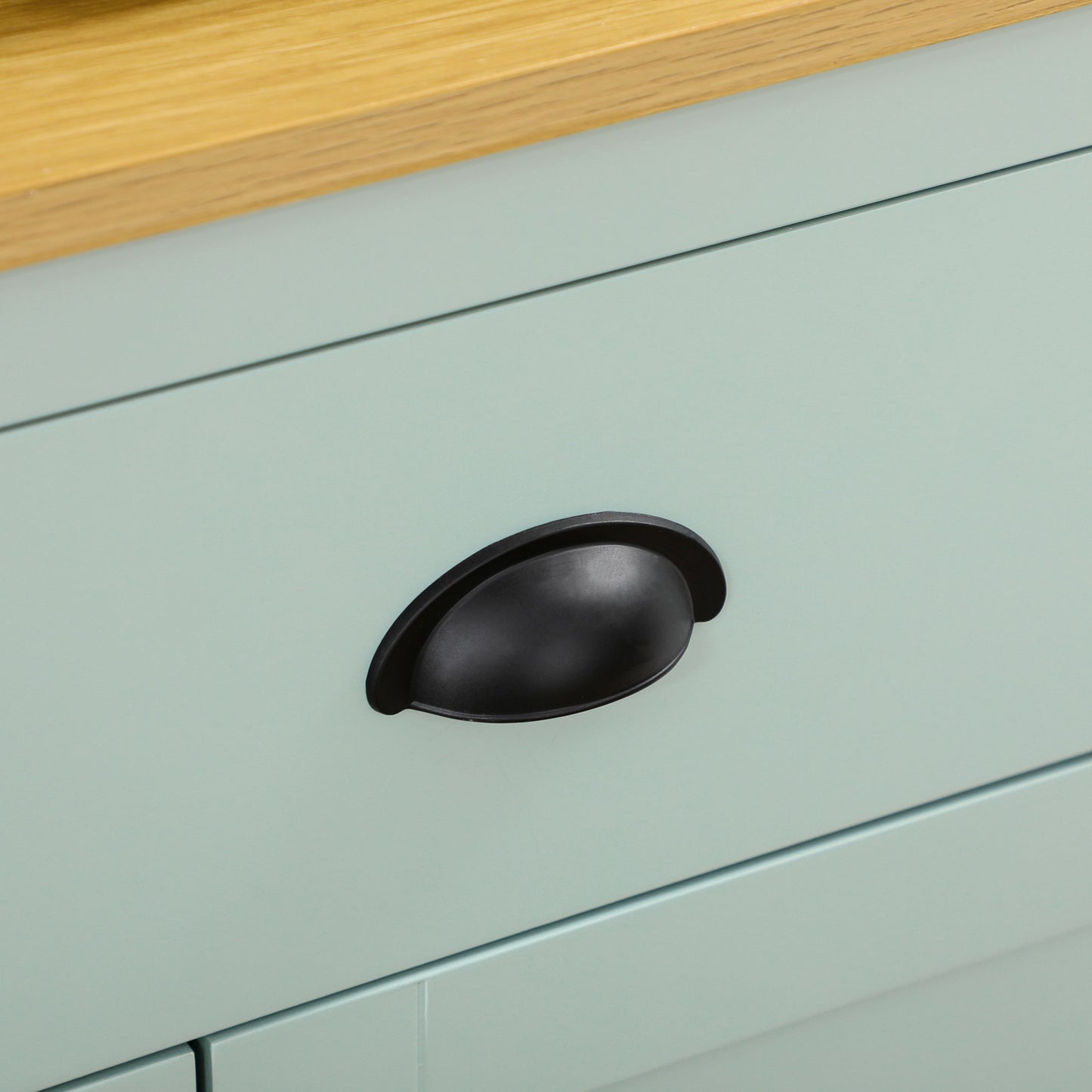 Close-up of a light blue kitchen hutch drawer with a black cup pull handle and natural wood countertop.