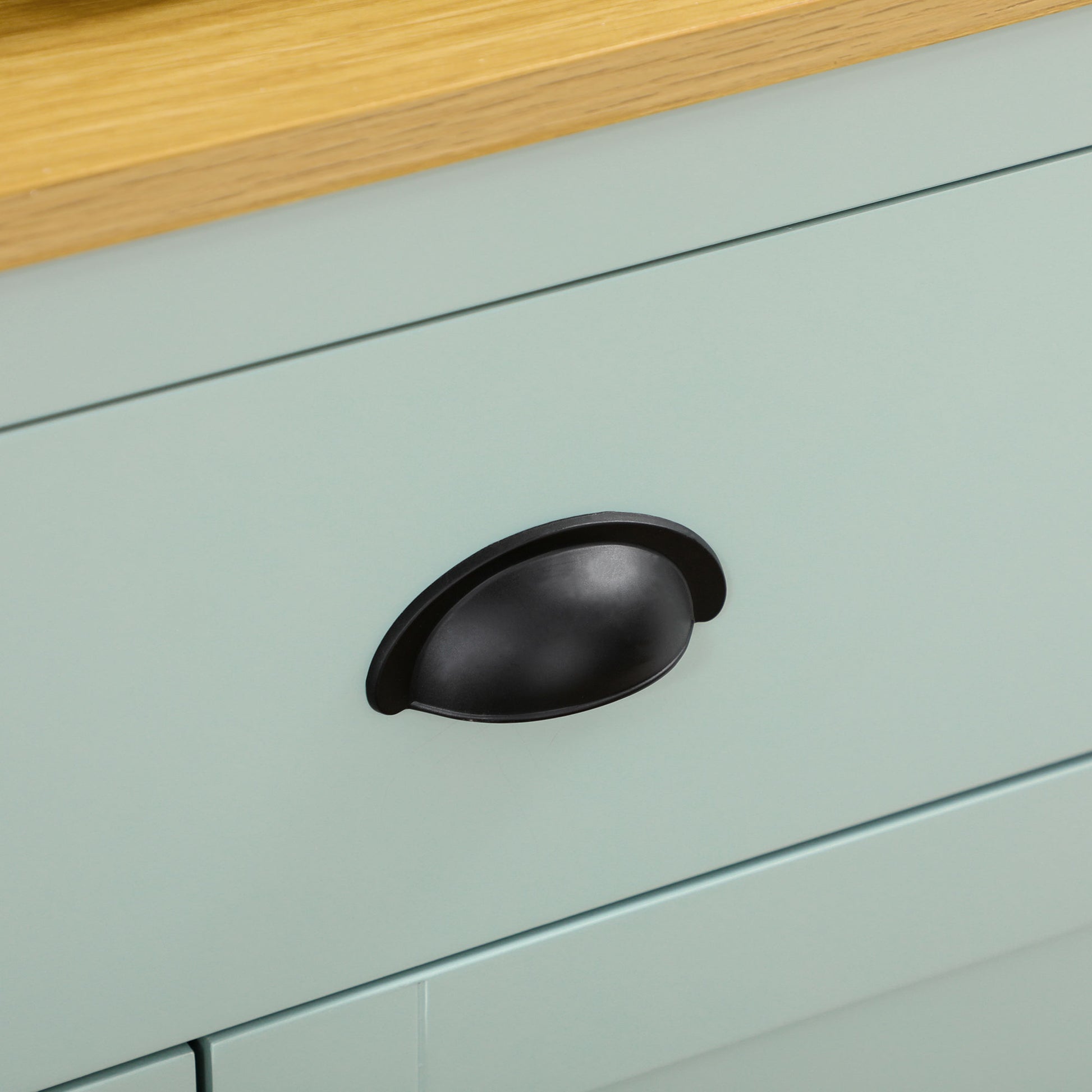Close-up of a light blue kitchen hutch drawer with a black cup pull handle and natural wood countertop.