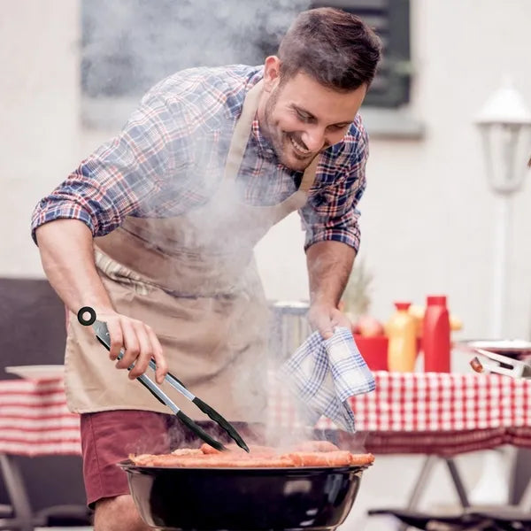 Smiling man in apron grilling sausages with black and silver tongs.