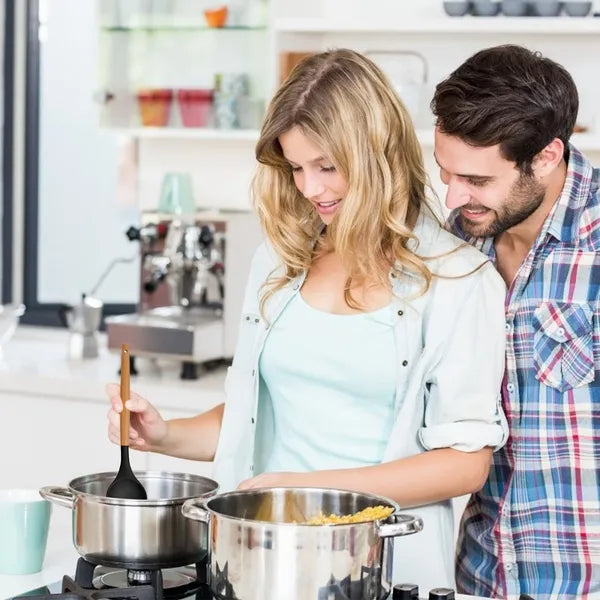 A couple cooking in a modern kitchen, using a black silicone spatula with a wooden handle in a pot.
