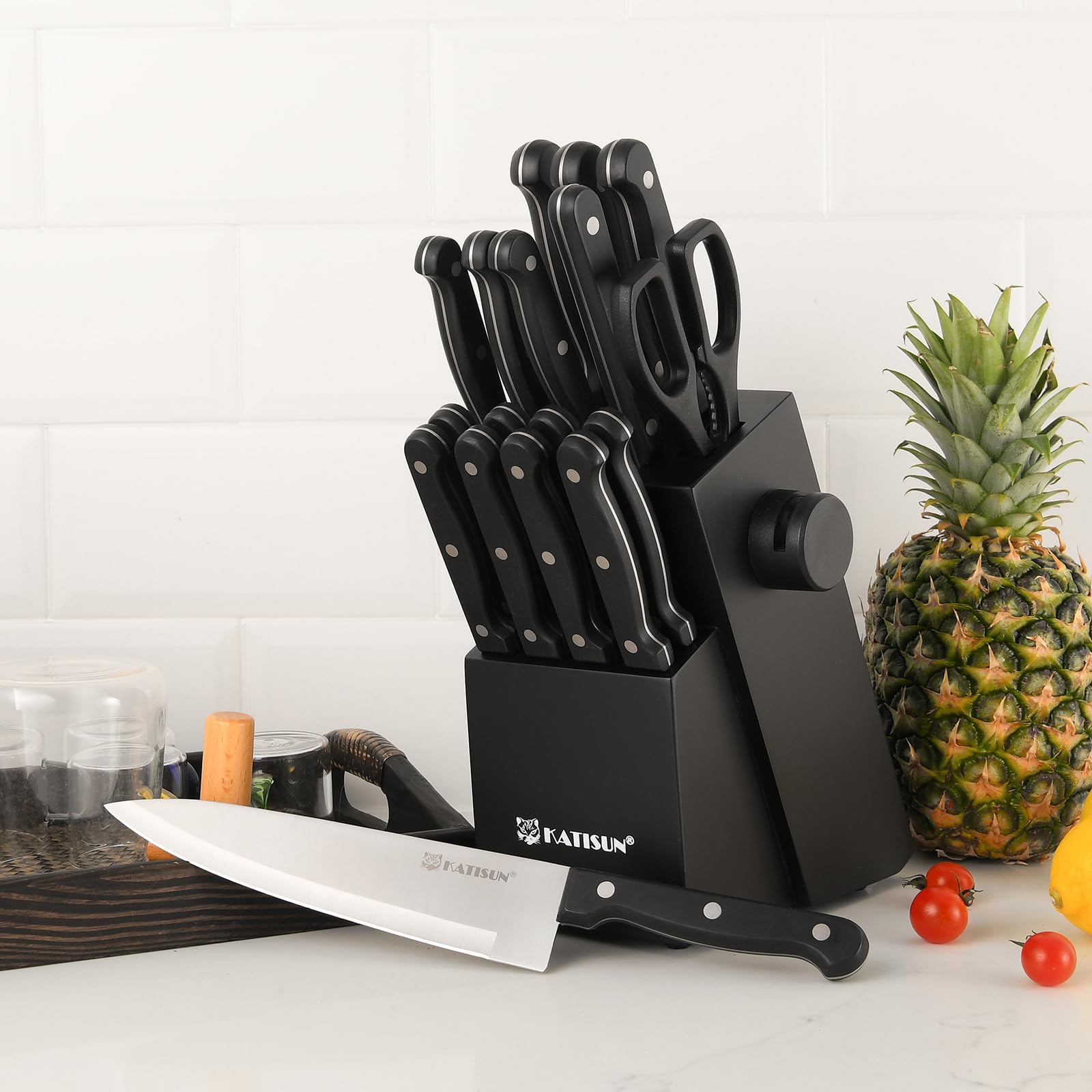 Black 9-piece German steel knife set in a modern block with sharpener, shown with a chef's knife, pineapple, and tomatoes.