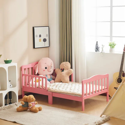 Pink wooden toddler bed with vertical plank headboard, side rails, and low-to-ground design.