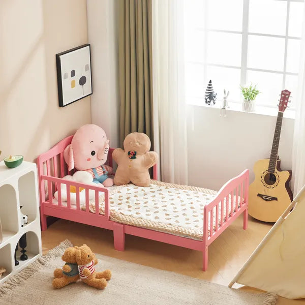Pink wooden toddler bed with vertical plank headboard, side rails, and a patterned blanket.