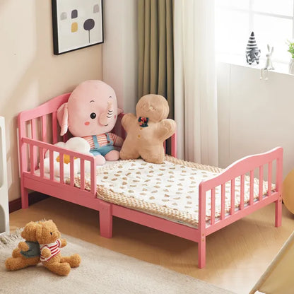 Pink wooden toddler bed with vertical plank headboard, side rails, and a patterned blanket.
