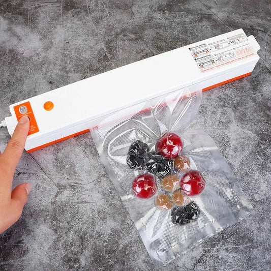 White and orange automatic vacuum sealer with a hand pressing a button, sealing a bag of fruit.