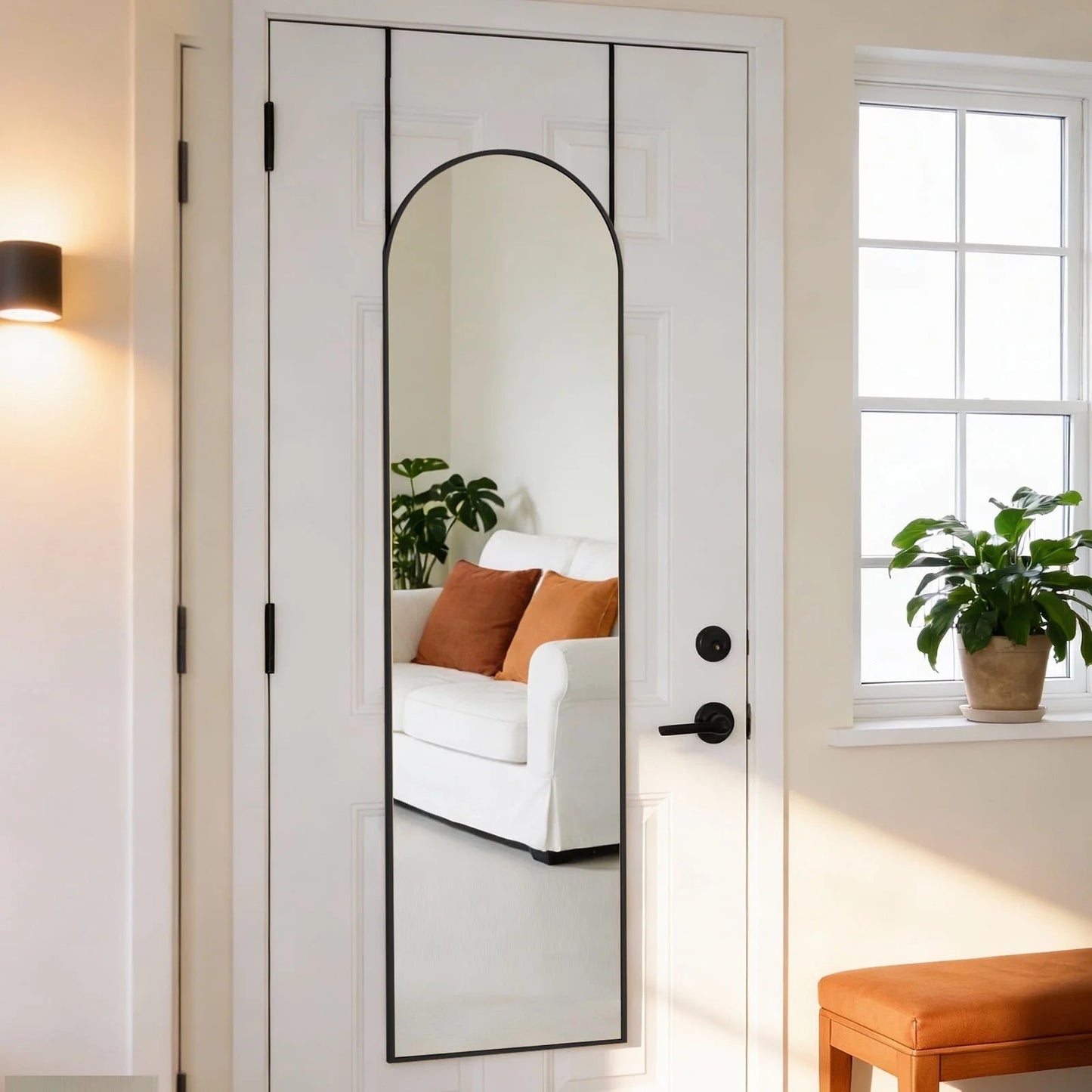 Black arched full-length mirror with a slim aluminum frame hanging over a white door.