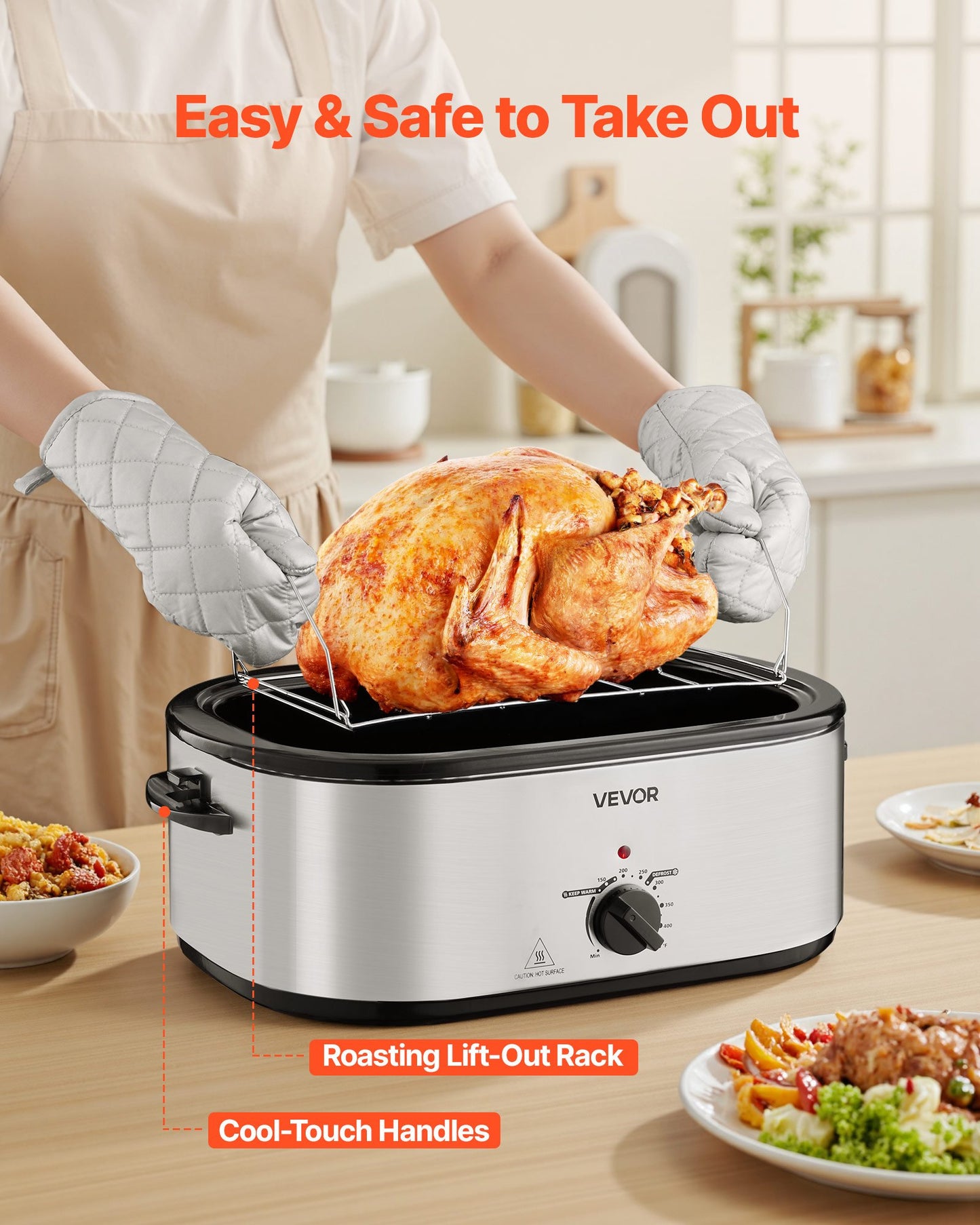 Silver 24QT VEVOR roaster with a golden roasted turkey on a lift-out rack, held by a person in oven mitts.