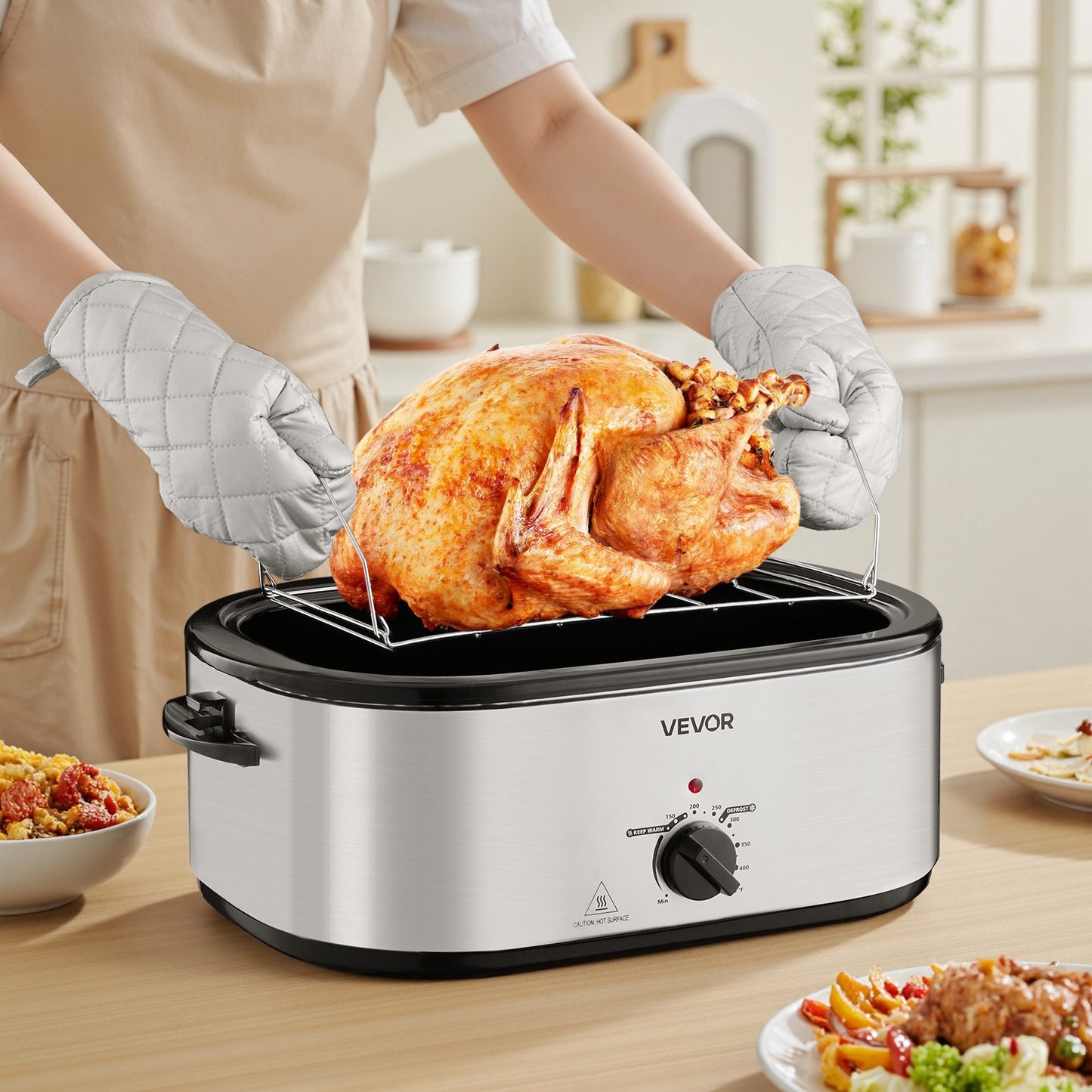 Stainless steel VEVOR 24QT roaster with a golden brown turkey on a rack, held by oven mitts.