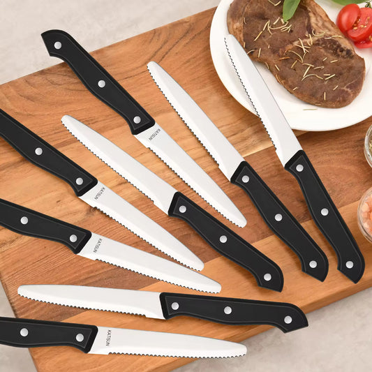 Black-handled KATSUN high-carbon stainless steel knife set on a wooden board with steak and tomatoes.