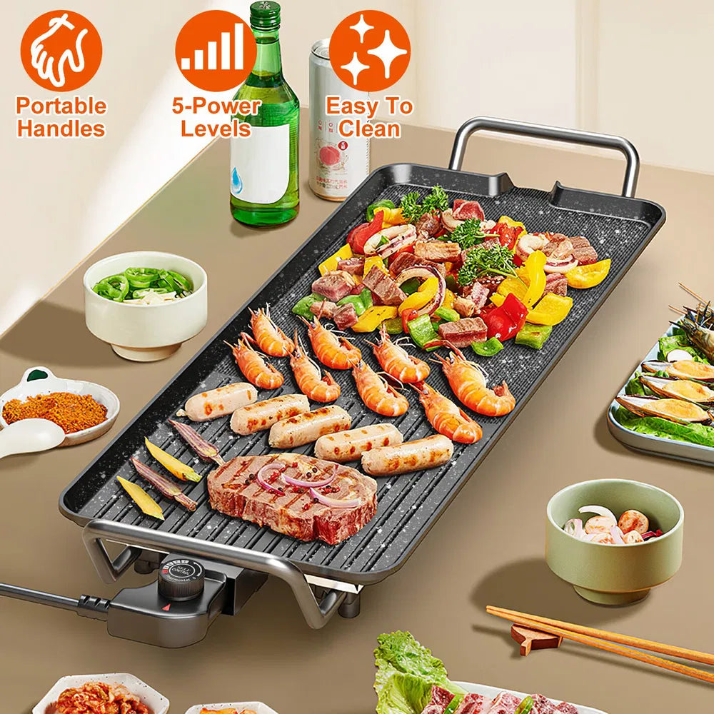 Black electric griddle with portable handles, cooking shrimp, steak, and vegetables, on a table.