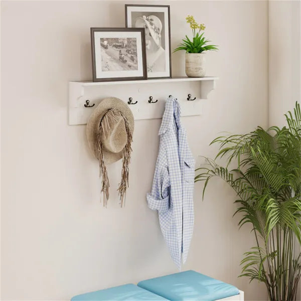 White entryway shelf with six black hooks, holding a hat and shirt, with framed art and a plant on top.