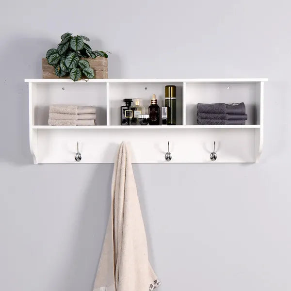 White wooden wall-mounted storage shelf with three compartments, three silver dual hooks, and a towel hanging.